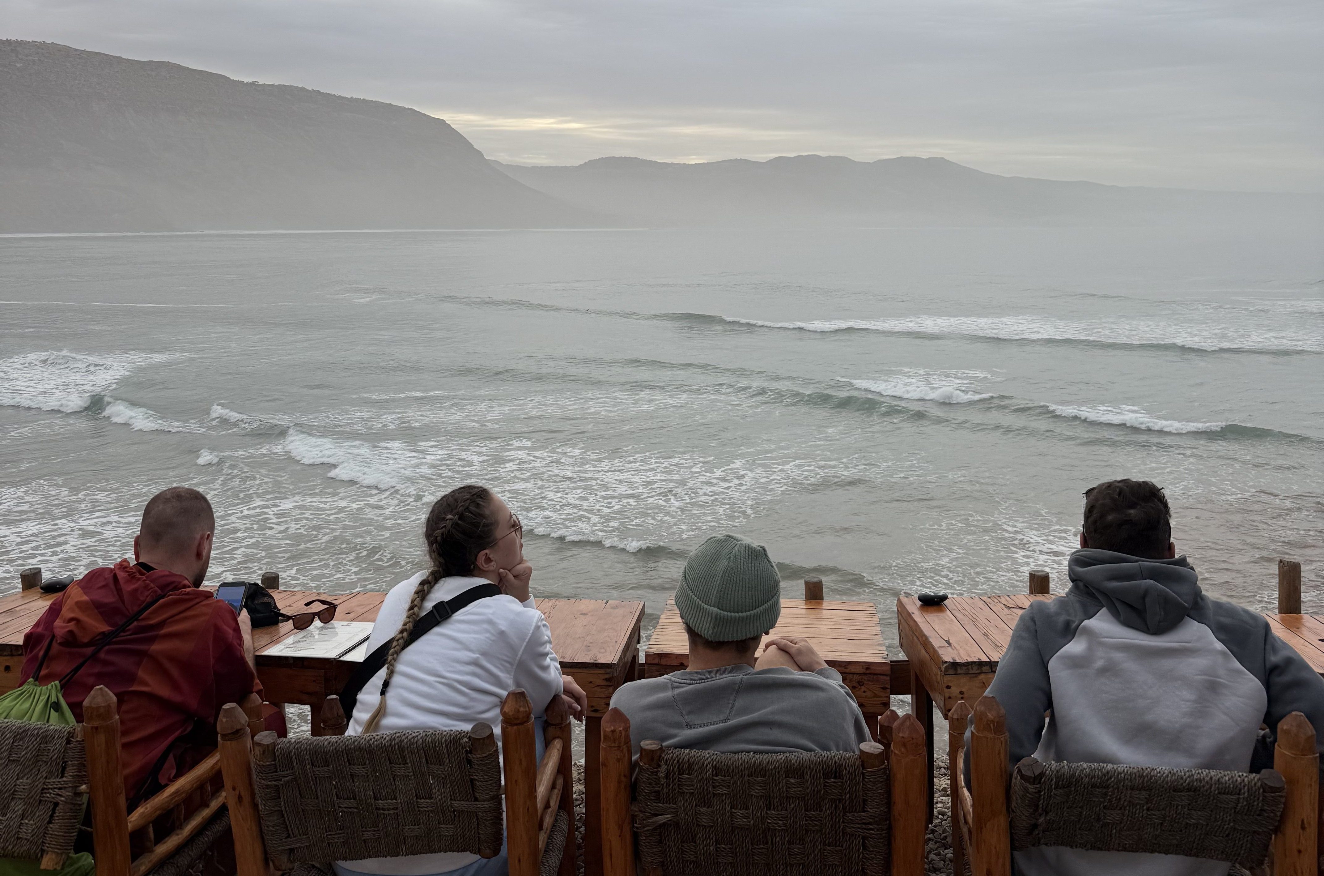 Four surfers sitting on a cliff overlooking Imsouane Bay, Morocco